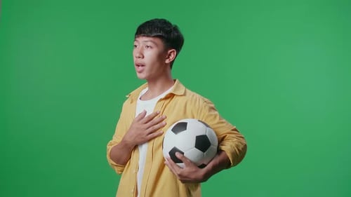 Side View Of Asian Boy With A Ball Singing National Anthem While Cheering Soccer On Green Screen