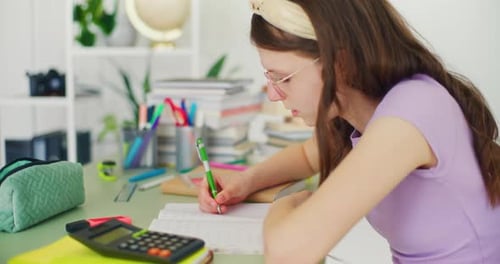 Young Student Writes in a Notebook Does Her Homework and Studies for School