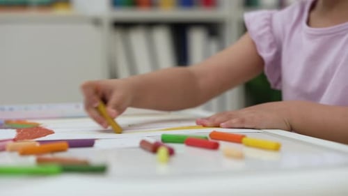 close up preschool child girl drawing and painting with colorful oil pastels on paper at home
