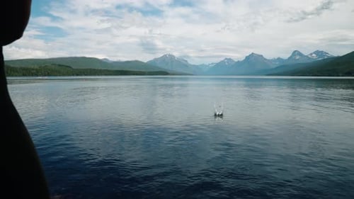 Girl skipping rock in slow motion on glacial lake at Glacier National Park with mountain range backd