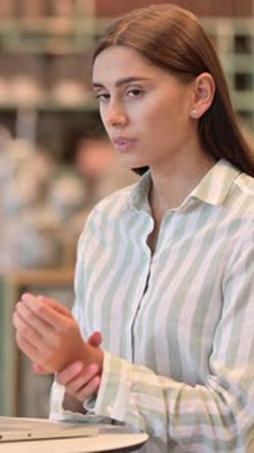 Young Latin Woman with Laptop having Wrist Pain in Cafe, vertical video