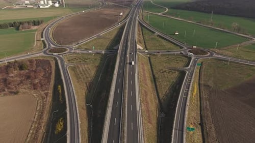 A high-angle aerial view of a highway interchange surrounded by agricultural land. Multiple roads,