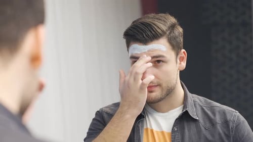 Man Applies Facial Mask in Mirror at Home