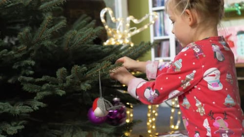 Girl Decorates Christmas Tree with Ornaments at Home