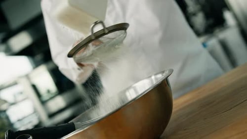 chef is sifting flour to the cooking bowl in a professional kitchen, making pancakes in a restaurant