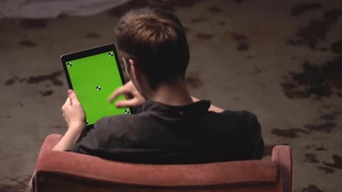 Young Man Using Tablet with Green Screen While Sitting on Armchair