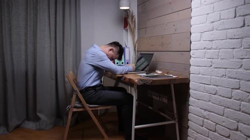 Male Professional in a Business Shirt and Dark Trousers Sleeping Face Down on an Open Laptop at a