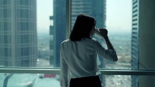 Young Businesswoman Drinking Coffee and Admire View From Window in Office 30s