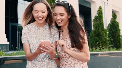 Two Young Women Laughing at Smartphone in City