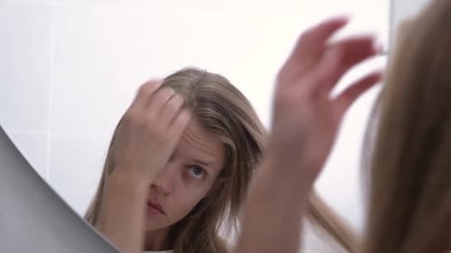 Haircare Concept. Woman Brushing Her Hair With Comb While Standing Near Mirror In Bathroom