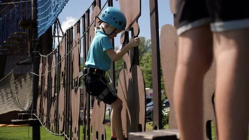 A Boy in a Helmet and Climbing Equipment Climbs a Rope Park in Summer