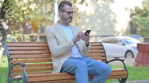 Man Using Smartphone Sitting on Park Bench