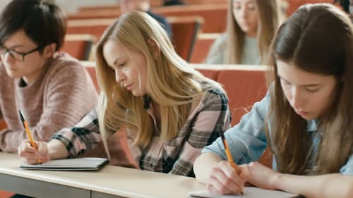 Reihe multiethnischer Schüler im Klassenzimmer, die Prüfung/Testen/Schreiben in Notizbücher ablegen. Strahlend jung