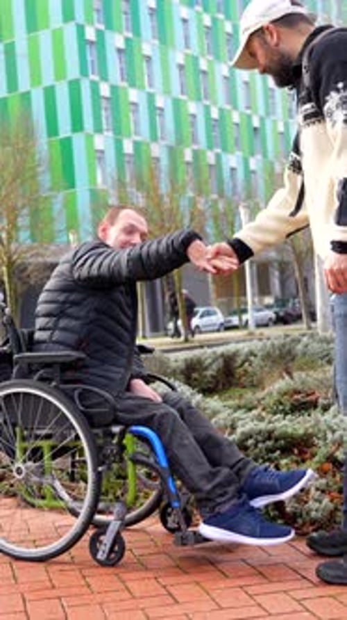 Man Pushes Friend in Wheelchair Along Urban Path