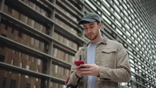 Jeune homme utilisant un téléphone portable dans une ville urbaine moderne, étudiant universitaire heureux souriant sur le campus
