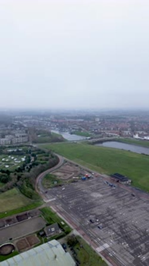 Vista aérea de un gran estacionamiento, campos verdes cercanos, un río y un área urbana con edificios