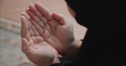 Eine asiatische muslimische Frau im schwarzen Hijab betet mit erhobenen Händen als Segen für Gott.