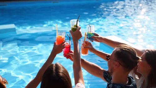 Friends raise drinks at a sunny poolside party