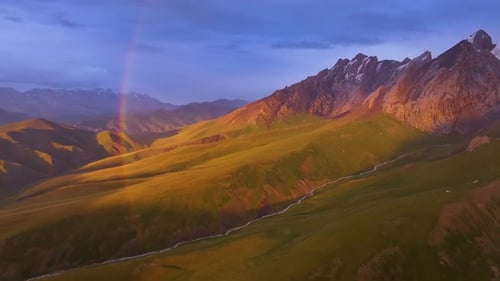 Rainbow over a green mountain valley with a winding river