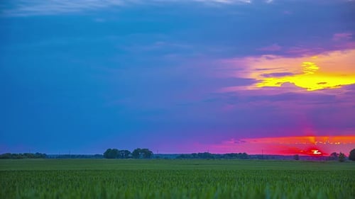 Timelapse of a colorful sunset over a field, the sun hidden behind the clouds