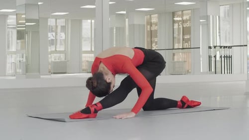 Ballerina stretching her leg on a mat in a white dance studio