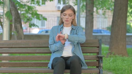 Young Woman Using Smartwatch while Sitting on Bench in Park