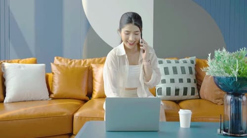 Woman Talking on Cell Phone Using Laptop at Home