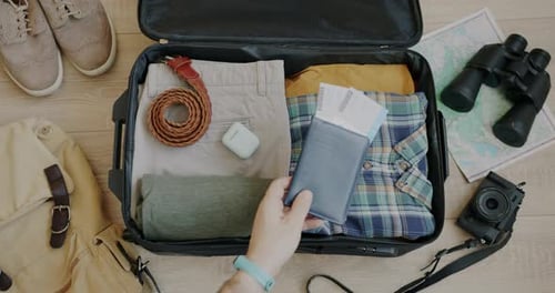 Top View of Hand Putting Passport and Plane Tickets in Suitcase Packing Bag for Vacation