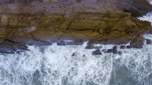 Top aerial drone view of waves crashing on rocky coastline. Blue ocean.