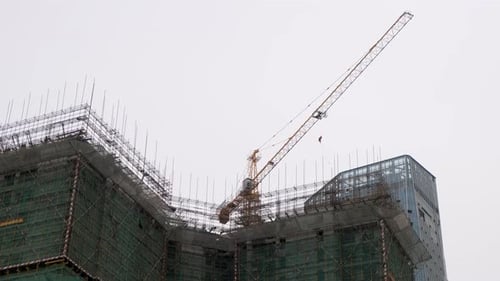 Grúa torre amarilla que opera en lo alto de un enorme rascacielos en construcción, con una amplia
