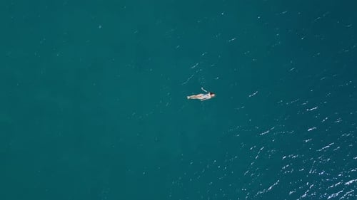 A câmera se move sobre a garota deitada nas ondas em águas abertas