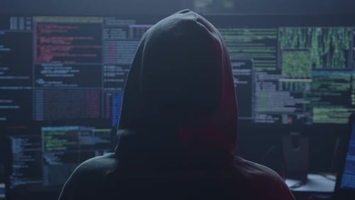 Un hacker se sienta en una habitación oscura rodeado de pantallas que muestran datos complejos