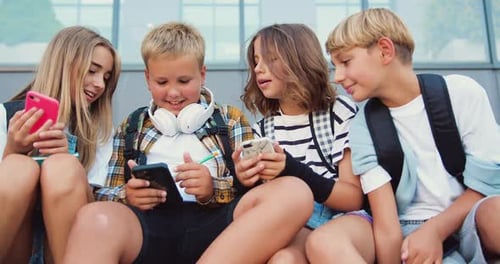 Cheerful group of four elementary school students sitting on stairs in the schoolyard