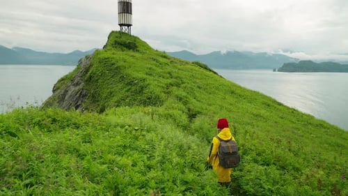 Young Adult Woman Traveler Walking In Beautiful Landscape With Lighthouse On Cape On Ocean Coast