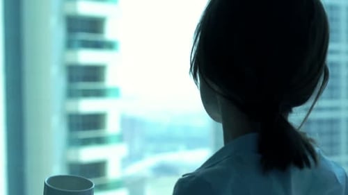 Young businesswoman enjoys morning coffee and city view from office window