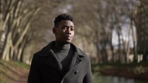 Pensive young African man walking outside in city park nature during winter season