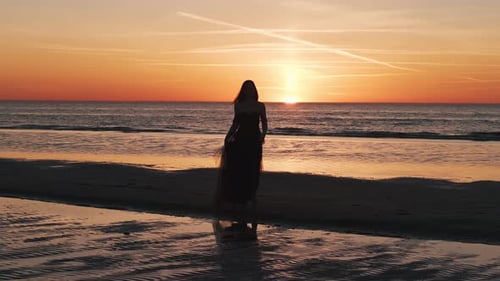 Happy Beautiful Woman in a Long Black Dress Enjoying Beautiful Sunset on the Beach in California