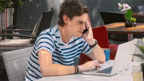 Young Man Working on Laptop Talking on Phone