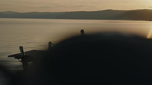 Fernblick auf eine Touristin, die auf dem Pier spaziert und den ruhigen Sonnenuntergang über einem ruhigen Berg genießt