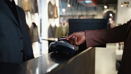 Afroamerikanischer Mann im Bekleidungsgeschäft, der kontaktlos mit Kreditkarte bezahlt
