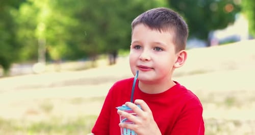 A Child Drinks Soda Beverage and Eats Chips Outdoors in a Park