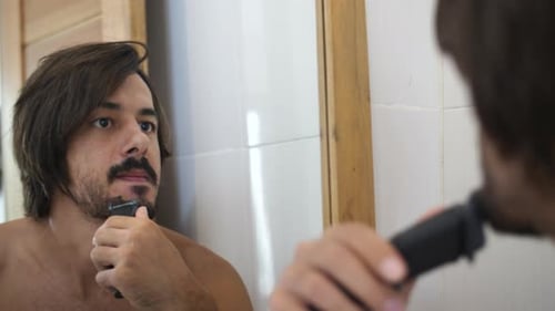 Man Trimming Beard with Electric Razor in Bathroom