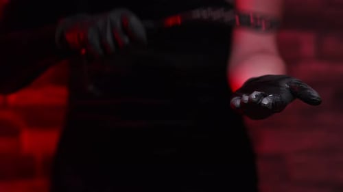 Close-up of female hands in black gloves holding a BDSM whip on a red background. Hits his hand with
