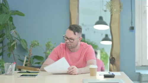 Man in Office Reviews Documents, Reacts with Stress