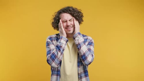 Man Rubs Temples in Pain Against Yellow Background