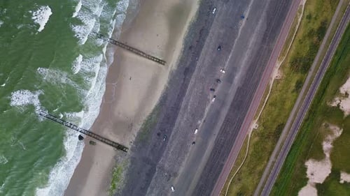 Aerial view of a shoreline where ocean waves meet sandy beach and rocky breakwaters.