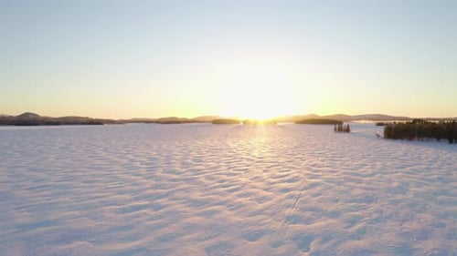 Aerial view flying across vast sunlit frozen Scandinavian terrain towards wintry sunrise horizon