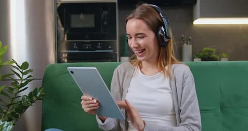 Hermosa chica estudiante con cabello largo en auriculares sentada en casa en el sofá y pasa el tiempo libre
