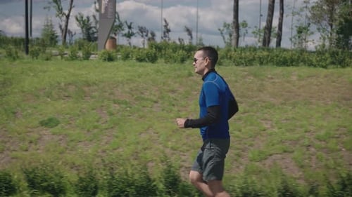 A Successful and Selfconfident Young Man Runs Through a Beautiful and Wellmaintained City Park