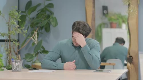 Stressed Man Rubbing Eyes at Workplace